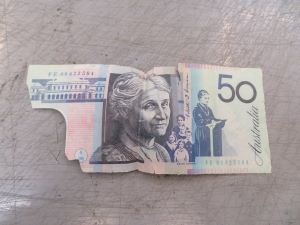 A faded $50 polymer banknote with tears and the clear window section missing.